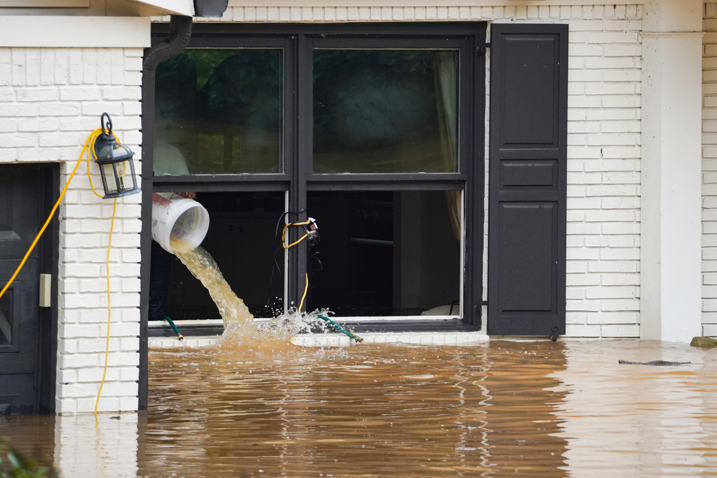 La gente lanza cubos de agua fuera de una casa como las calles y las casas están inundadas cerca de Peachtree Creek después de huracán Helene trajo fuertes lluvias durante la noche el 27 de septiembre de 2024 en Atlanta, Georgia. (Foto de Megan Varner/Getty Images)