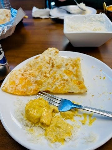 A plate with shrimp korma over rice and a piece of the cheese naan.
