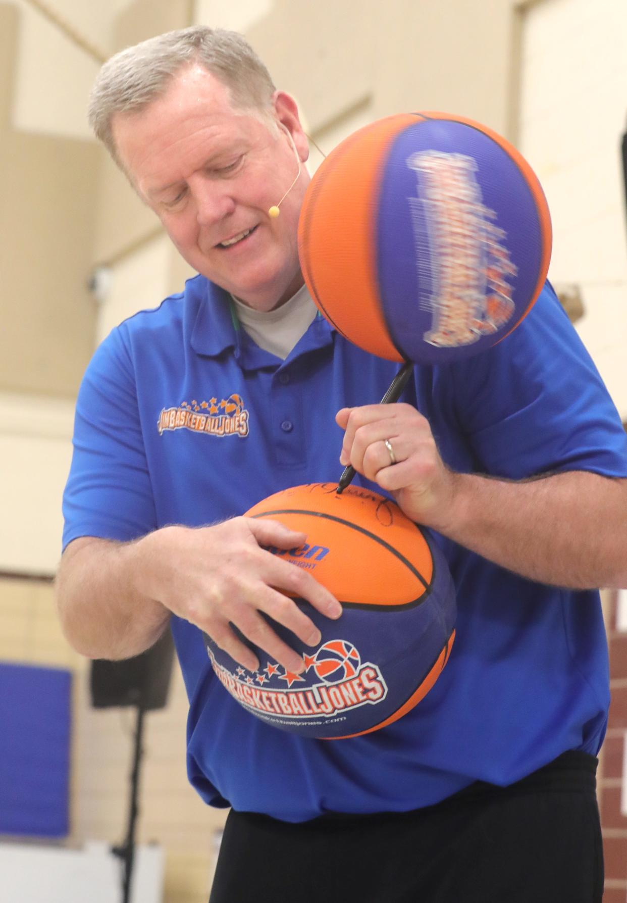 Jim Basketball Jones signs a basketball while balancing a spinning ball on his pen during an assembly for students at Herberich Primary School on Tuesday in Fairlawn.