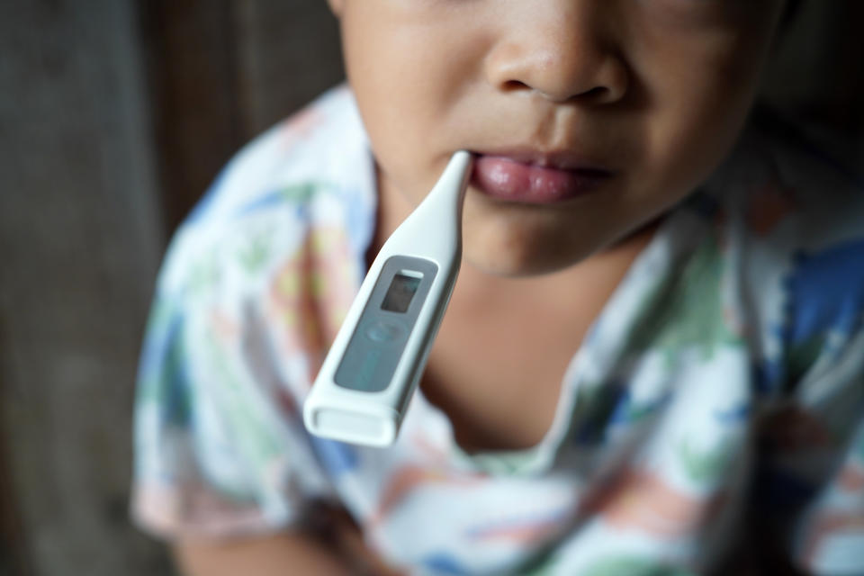 A sick child who has a thermometer in their mouth to check their temperature. (Photo via Getty Images)