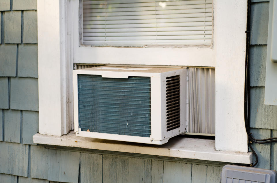 A window-mounted air conditioning unit installed in a home's exterior with blinds partially closed