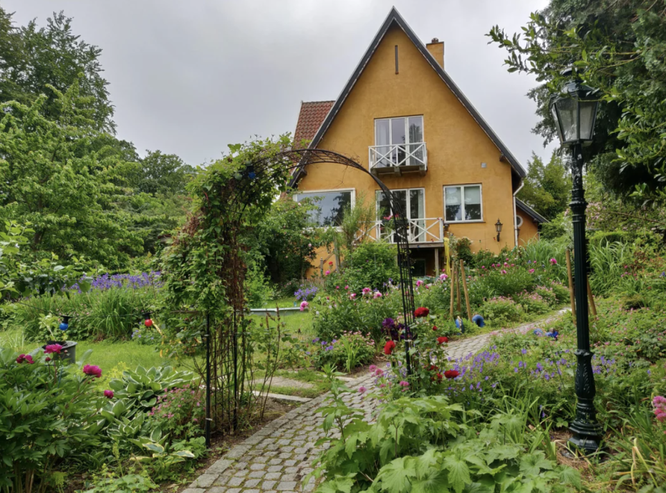 A quaint house with a garden pathway and an arch covered with vines