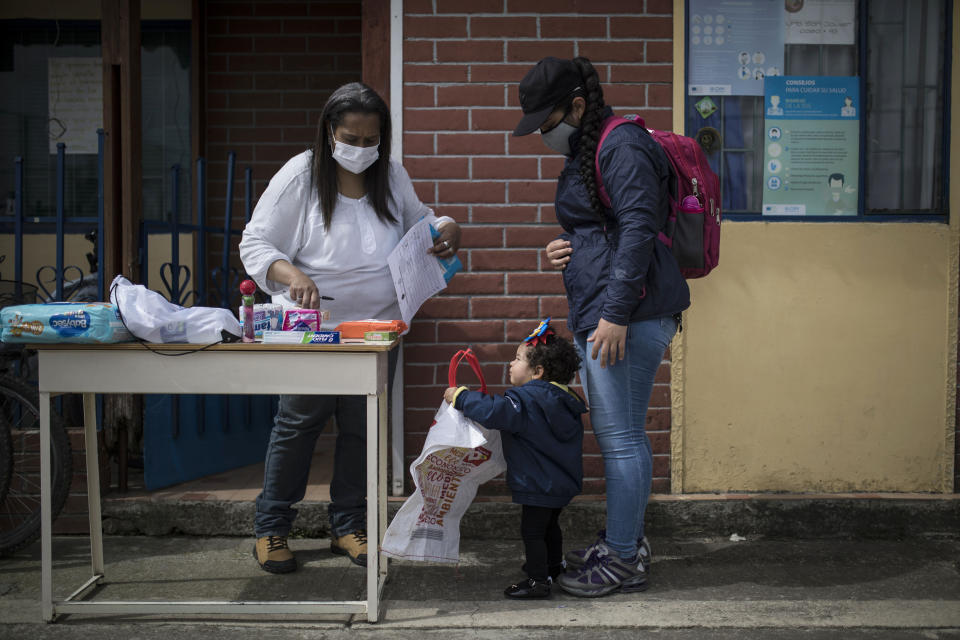 Colombian resident Alba Rada gifts toiletries and food to Venezuelan migrant Rosmira Camacho and her child, outside Rada's home where she runs her foundation, Radaber, in Tocancipa, Colombia, Tuesday, Oct. 6, 2020. For many Venezuelan migrants arriving to Colombia, the prospect of earning even less than the minimum wage is a boost, currently worth around $260 a month, far higher than Venezuela’s $2. (AP Photo/Ivan Valencia)