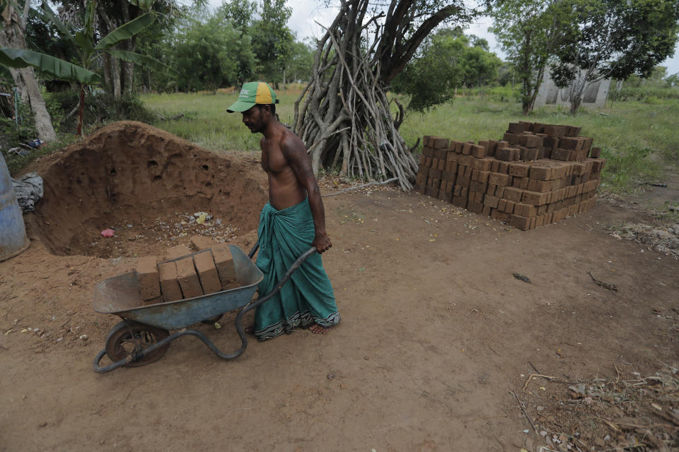 A Sri Lankan Telugu man Masannage Sunil pushes a wheel barrow loaded with bricks in Nachchikulama, Sri Lanka, Wednesday, June 17, 2020. Sri Lanka's Telugu community, whose nomadic lifestyle has increasingly clashed with the modern world, is facing another threat that could hasten its decline: the COVID-19 pandemic. (AP Photo/Eranga Jayawardena)