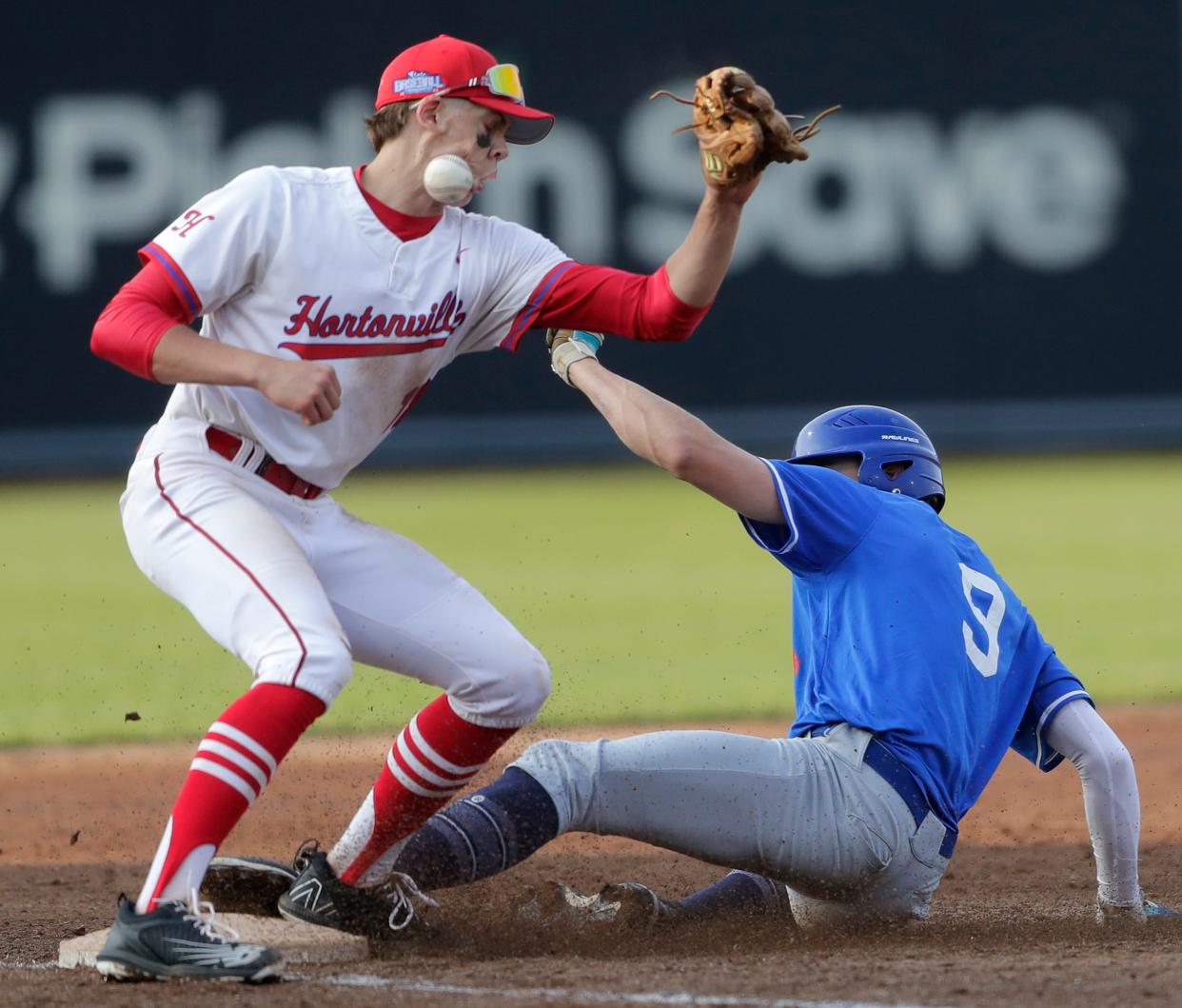 Hortonville High School's Brett Sommer (18) is hit by the ball as Whitefish Bay High School's J.D. Dix (9) slides into third base during their Division 1 championship baseball game in the WIAA state baseball tournament June 15, 2023, at Neuroscience Group Field at Fox Cities Stadium in Grand Chute, Wis. Whitefish Bay defeated Hortonville 5-1. This photo earned The Reporter first place for Sports Action Photo.