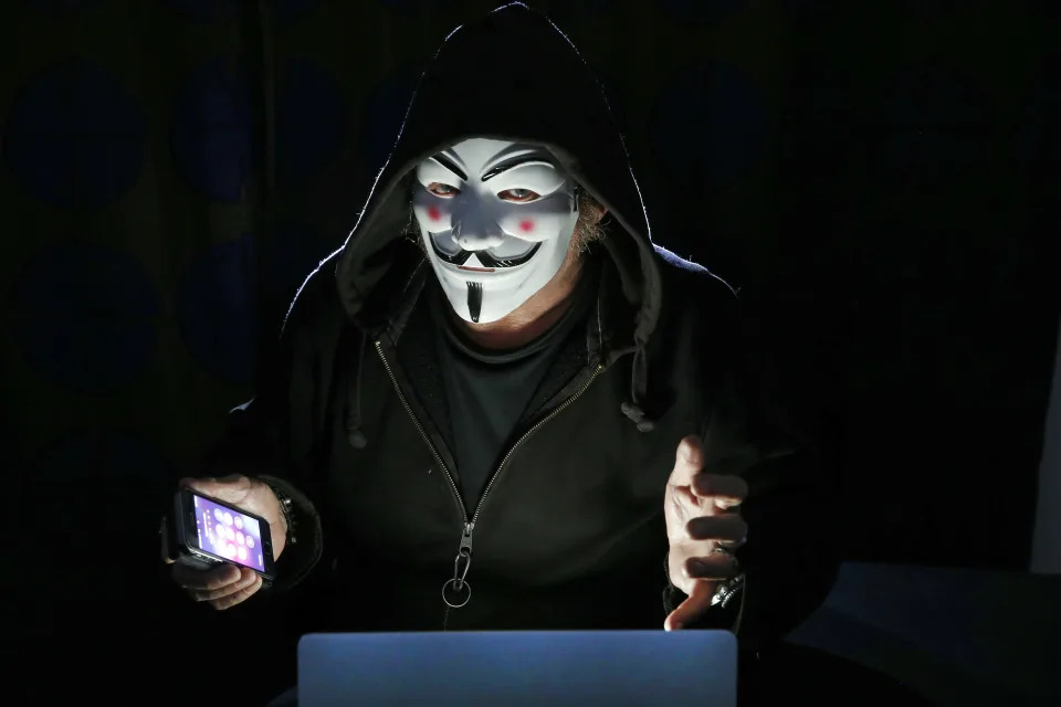PARIS, FRANCE - DECEMBER 27: In this photo illustration, a hacker with an Anonymous mask on his face and a hood on his head uses a computer on December 27, 2019 in Paris, France. In IT security, a hacker is an IT specialist, who is looking for ways to bypass software and hardware protections. Hackers are generally intelligent programmers who seek to manipulate or modify a computer system or network. (Photo by Chesnot/Getty Images)