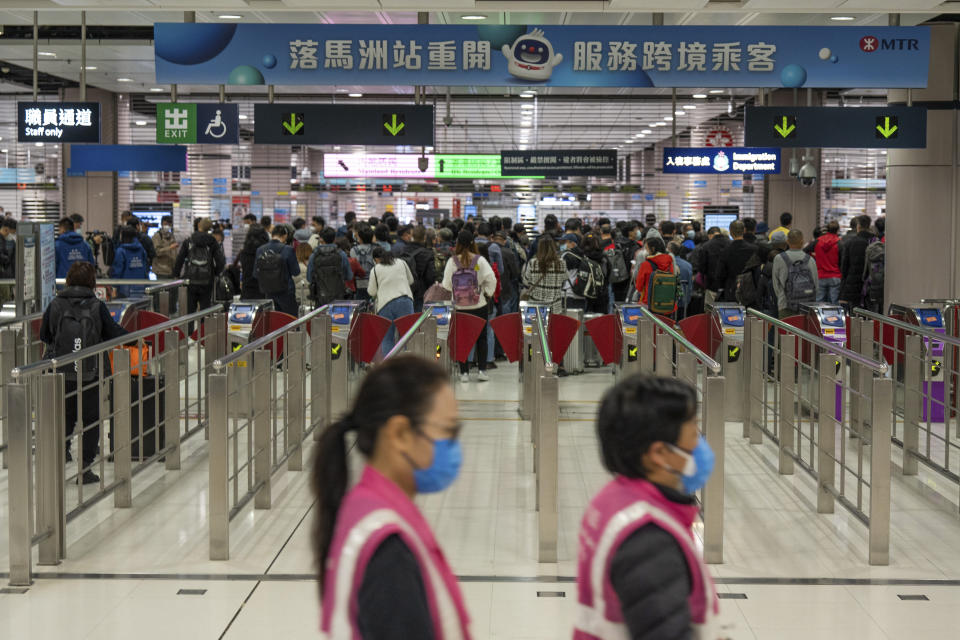 Workers wearing face masks walk by as travelers wait at the departure hall of the Lok Ma Chau station following the reopening of crossing border with mainland China, in Hong Kong, Sunday, Jan. 8, 2023. Travelers crossing between Hong Kong and mainland China, however, are still required to show a negative COVID-19 test taken within the last 48 hours, a measure China has protested when imposed by other countries. (AP Photo/Bertha Wang)