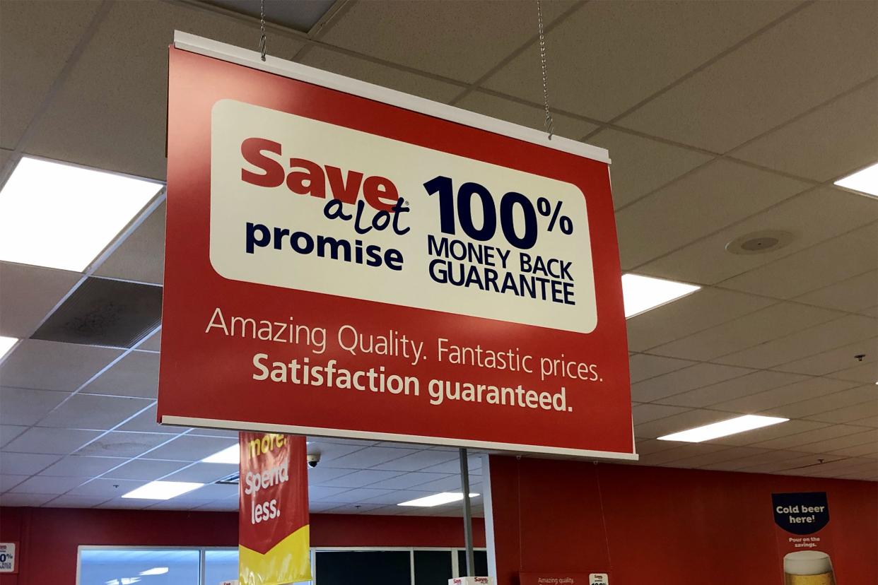 Money back guarantee sign hanging from ceiling at Save A Lot, with windows, ceiling and other hanging signs in the backgound