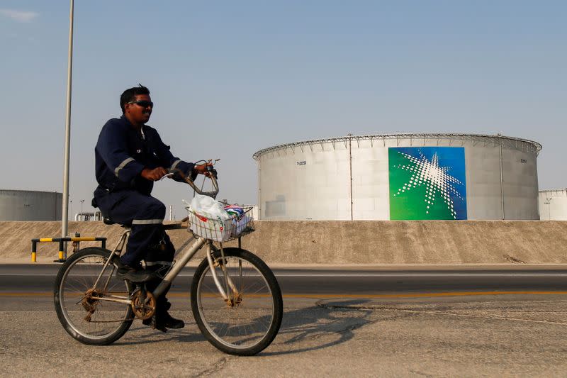 FILE PHOTO: An employee rides a bicycle next to oil tanks at Saudi Aramco oil facility in Abqaiq