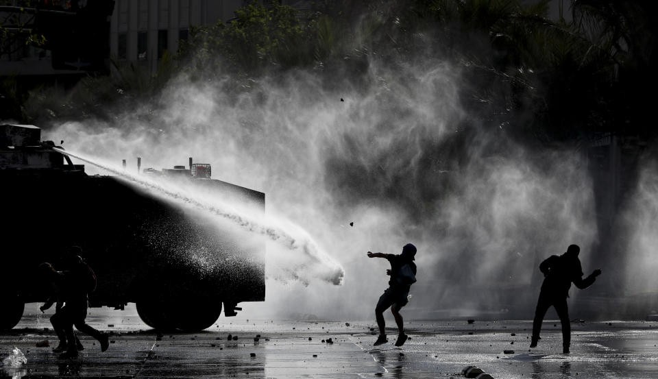 Demonstrators clash with a police water cannon during an anti-government protest in Santiago, Tuesday, Nov. 5, 2019. Chileans have been taking to the streets and clashing with the police to demand better social services and an end to economic inequality, even as the government announced that weeks of demonstrations are hurting the country's economic growth. (AP Photo/Esteban Felix)