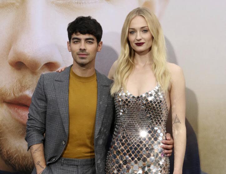 Joe Jonas wears a suit while putting his arm around wife Sophie Turner, who wears a glittering silver dress