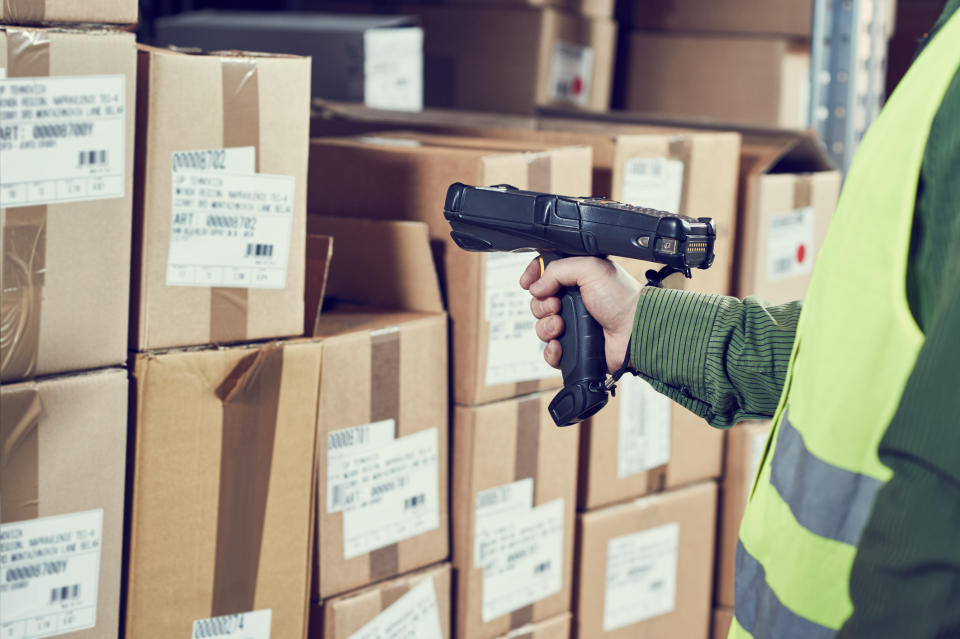 Warehouse worker scanning barcodes on one of many cardboard boxes.