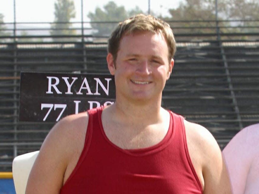 Ryan after losing weight smiling in a red tank top on a football field.
