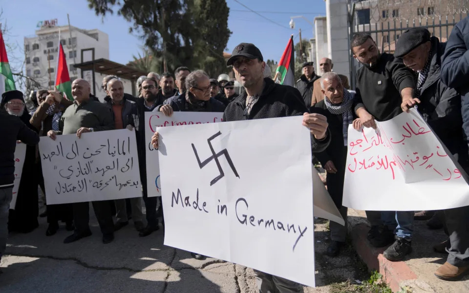 A Palestinian activist carries a Swastika poster  in protest at Germany's support for Israel