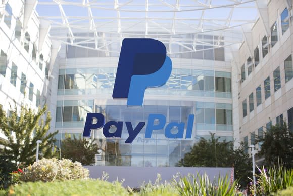 A blue PayPal sign on glass surrounded by shrubbery in front of its headquarters.