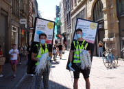 FILE - In this Aug. 5, 2020 file photo, face masks are offered to people in Amsterdam. The Netherlands’ two most populous cities have begun ordering people to wear face masks in busy streets. Wednesday, Sept. 9, new policy comes amid rising coronavirus infection rates. Despite the new order, many people in the Dutch capital’s famous red-light district still did not wear a mask (AP Photo/Mike Corder)