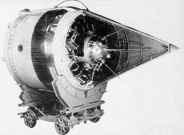 A conical spacecraft with four wheels on its side, a conical fairing cut in half to reveal a smaller chrome space probe with an antenna.