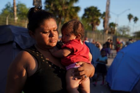 A Honduran asylum seeker carries her daughter in an encampment where they live near the Gateway International Bridge after being sent back under the "Remain in Mexico" program in Matamoros.