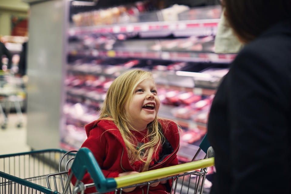 Happy smiling little girl sat in a shopping trolley while food shopping at the Supermarket