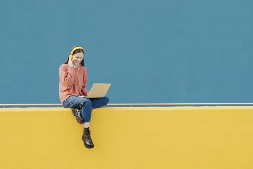 Woman wearing headphones smiles while sitting on illustrated wall.