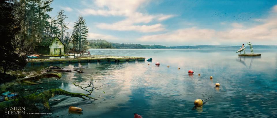 concept art of a dock in station eleven. it shows a derelict shack and overgrown shore, stretching out onto a green tinged wooden dock. there are still buoys chained together on a string extending into the water, and a float slightly out in the lake with a slide