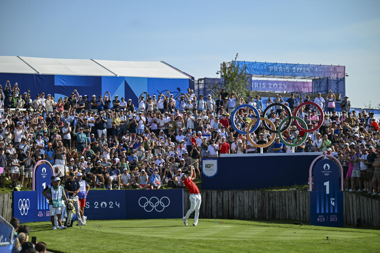 PARIS, FRANCE - AUGUST 01:  Scottie Scheffler of Team USA plays a shot from the first hole tee as fans look on beyond the rings during the first round of the Olympic men's golf competition on day six of the Olympic Games Paris 2024 at Le Golf National on August 1, 2024 in Saint-Quentin-en-Yvelines, France. (Photo by Keyur Khamar/PGA TOUR via Getty Images)