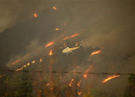 A helicopter drops water as firefighters battle a fast-moving California wildfire, so-called the "Colby Fire", in the hills of Glendora January 16, 2014. REUTERS/Gene Blevins