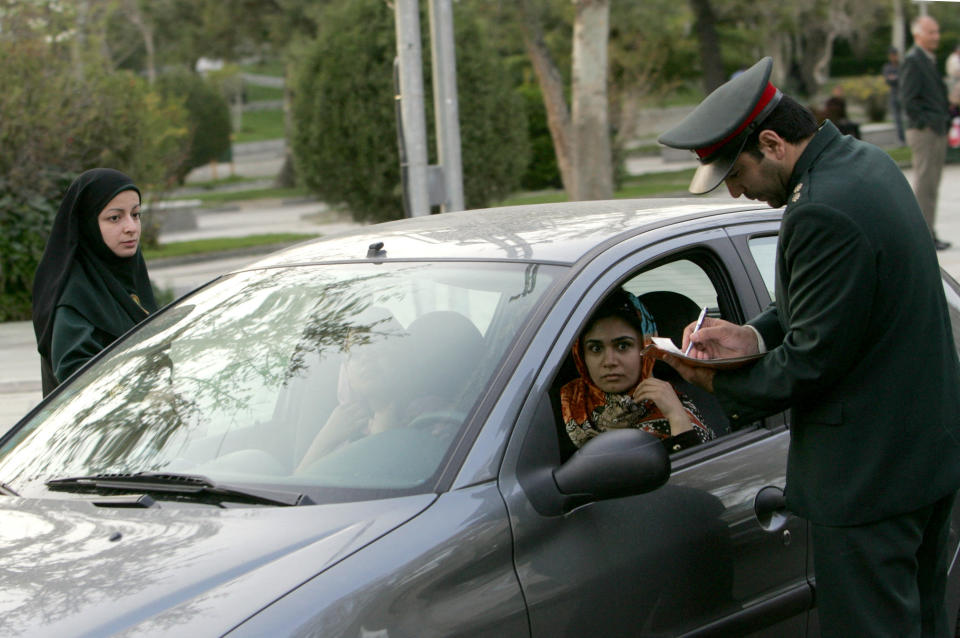 An Iranian police officer stops a car with a female driver and passenger.