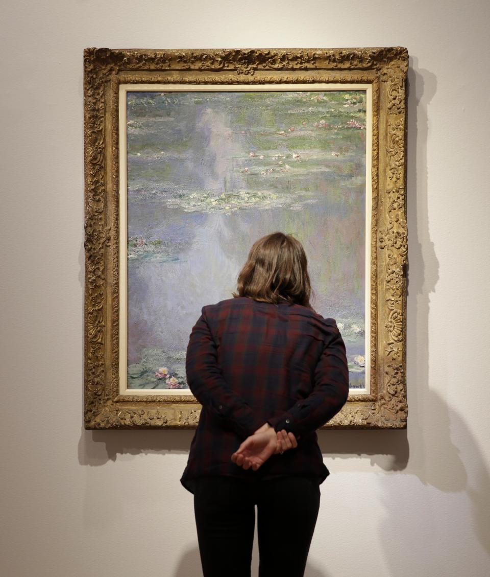 A woman gets a closer look at "Nympheas" by Claude Monet during an auction preview at Christie's in New York, Tuesday, May 6, 2014. Works from the estates of heiress Huguette Clark, Edgar Bronfman and other major collectors are leading New York City’s spring art auctions. The sale of impressionist and modern art begins Tuesday evening at Christie’s. The auction house says it expects to raise over $245 million. (AP Photo/Seth Wenig)