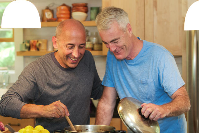 Senior gay male couple at home cooking together, affectionate and in love