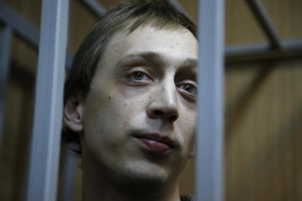 Pavel Dmitrichenko looks through bars as he stands in a cage at a court room in Moscow on Tuesday, Oct. 22, 2013. Bolshoi dancer Dmitrichenko goes on trial on Tuesday, on charges of organizing an acid attack against the ballet's artistic director, Sergei Filin. (AP Photo/Alexander Zemlianichenko)