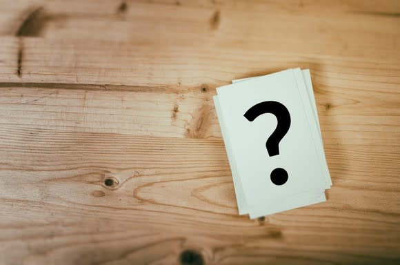 A small card of paper with a question mark on it sitting on a wooden table.