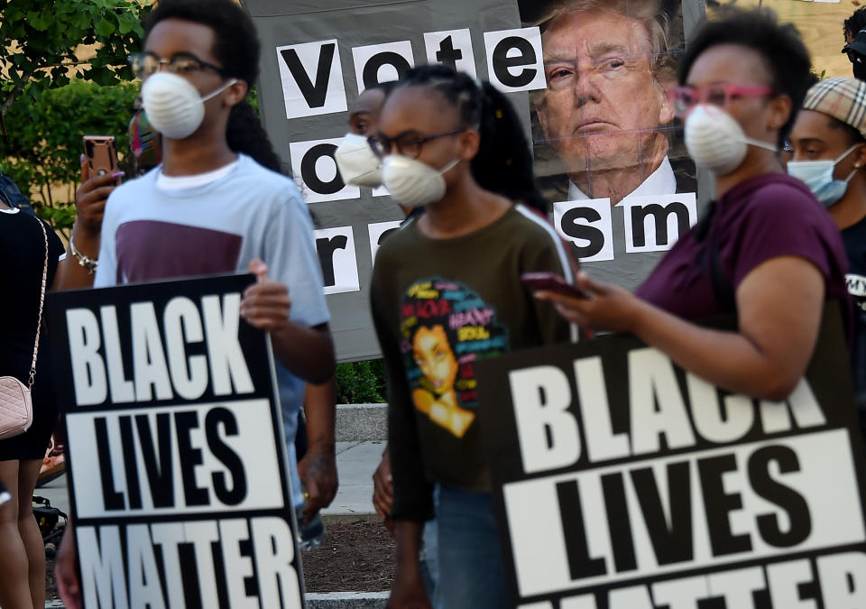 Demonstrators holding Black Lives Matter signs stand by a sign calling to vote out racism with a picture of President Donald Trump, during a peaceful protest against police brutality and the death of George Floyd, on June 7, 2020 in Washington, DC. (Olivier Douliery/AFP via Getty Images)