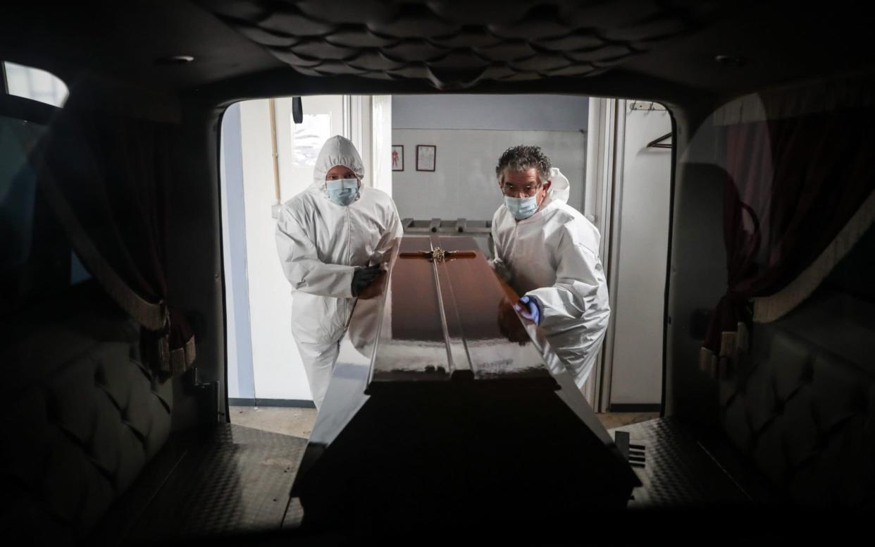 Two funerary workers load a coffin into a vehicle - MARIO CRUZ/EPA-EFE/Shutterstock