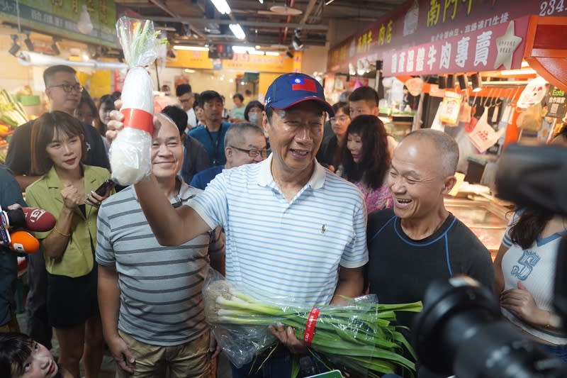 鴻海集團創辦人郭台銘（前中）11日前往台北市南門中繼市場，有攤商熱情送上象徵好彩頭的白蘿蔔。（中央社）