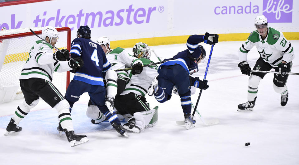 Dallas Stars goaltender Jake Oettinger, center, upends Winnipeg Jets' Vladislav Namestnikov, second from right, as Stars' Mason Marchment (27) looks for the loose puck during the first period of an NHL hockey match in Winnipeg, Manitoba, on Tuesday, Nov. 28, 2023. (Fred Greenslade/The Canadian Press via AP)