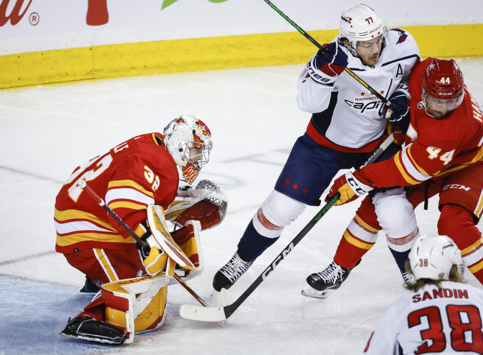 Washington Capitals forward T.J. Oshie (77) is checked by Calgary Flames defenseman Joel Hanley (44) as Flames goalie Dustin Wolf (32) looks on during second-period NHL hockey game action in Calgary, Alberta, Monday, March 18, 2024. (Jeff McIntosh/The Canadian Press via AP)