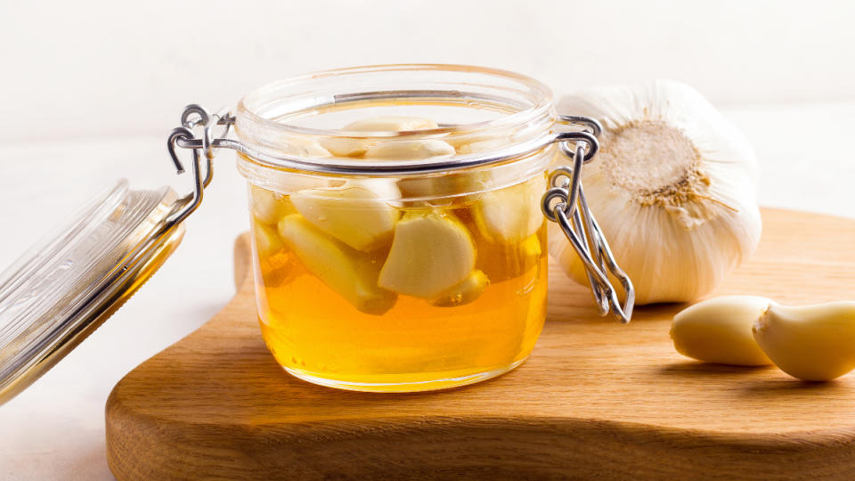 A wide glass jar with honey and garlic, which have health benefits, on a wood cutting board
