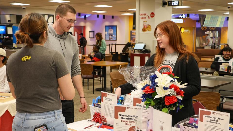 Kyndra Andres, right, a junior management major from Abilene, encourages West Texas A&M University students to place bids in a silent auction raising funds for Hope Lives Here.