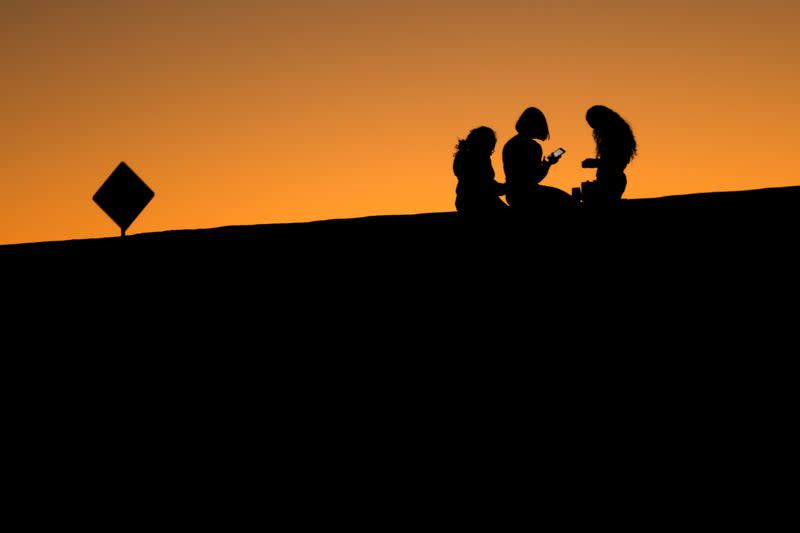 FILE PHOTO: Young girls look at their phones as they sit on a hillside after sun set in El Paso, Texas