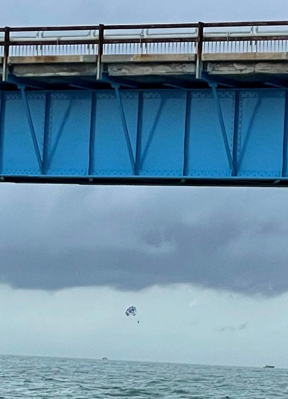 Tres personas cuelgan de un parasail en el viejo Seven Mile Bridge en los Cayos de la Florida, el lunes 30 de mayo de 2022, minutos antes de que una fuerte ráfaga de viento obligara al capitán de la embarcación que los remolcaba a soltarlos.