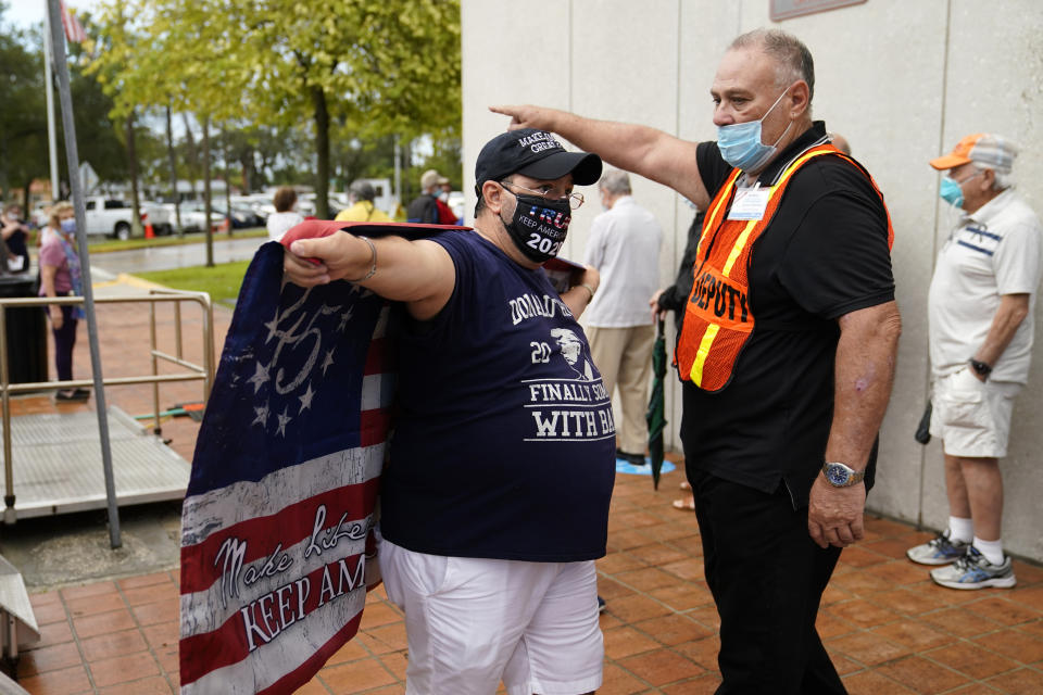 An election worker, right, asks Roland Linares, 50, left, to leave as he carries a flag in support of President Donald Trump outside of an early voting site, Monday, Oct. 19, 2020, in Miami. Florida begins in-person early voting in much of the state Monday. With its 29 electoral votes, Florida is crucial to both candidates in order to win the White House. (AP Photo/Lynne Sladky)