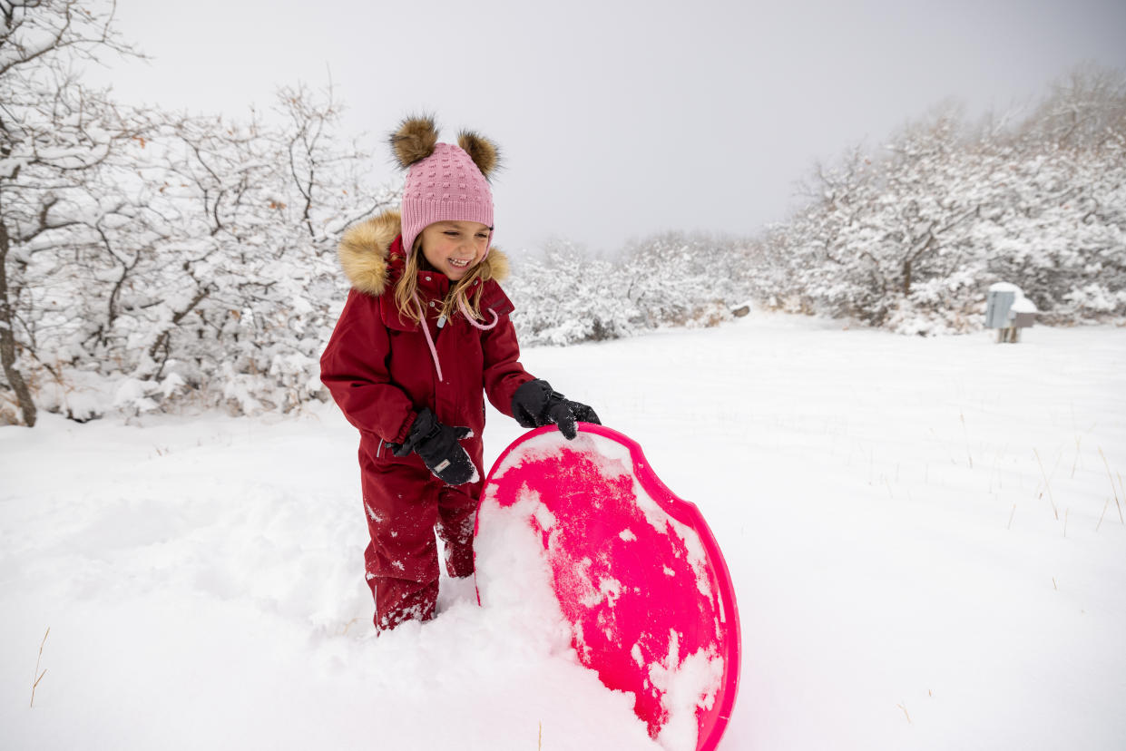 Small girl plays with snow sled.