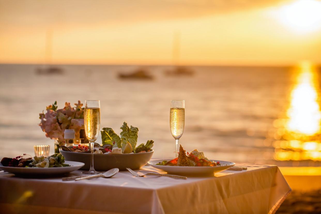 Romantic sunset dinner on the beach. Table honeymoon set for two with luxurious food, glasses of champagne drinks in a restaurant with sea view. Summer love, romance date on vacation concept.