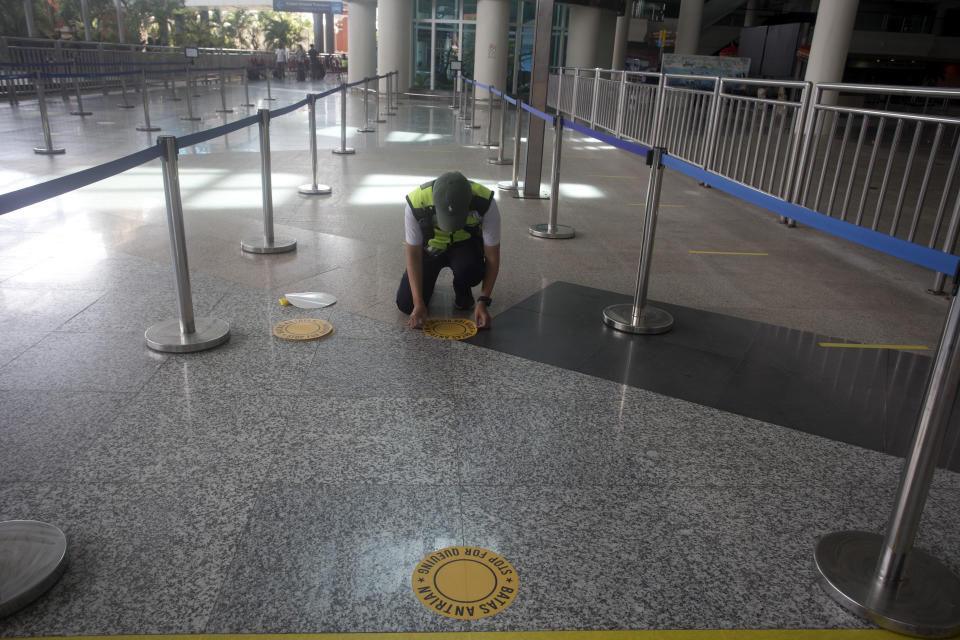 An airport worker marks queue line for the reopening of International Ngurah Rai Airport in Bali, Indonesia, Thursday, Oct. 14, 2021. The Indonesian resort island of Bali welcomed international travelers to its shops and white-sand beaches for the first time in more than a year Thursday - if they're vaccinated, test negative, hail from certain countries, quarantine and heed restrictions in public. (AP Photo/Firdia Lisnawati)