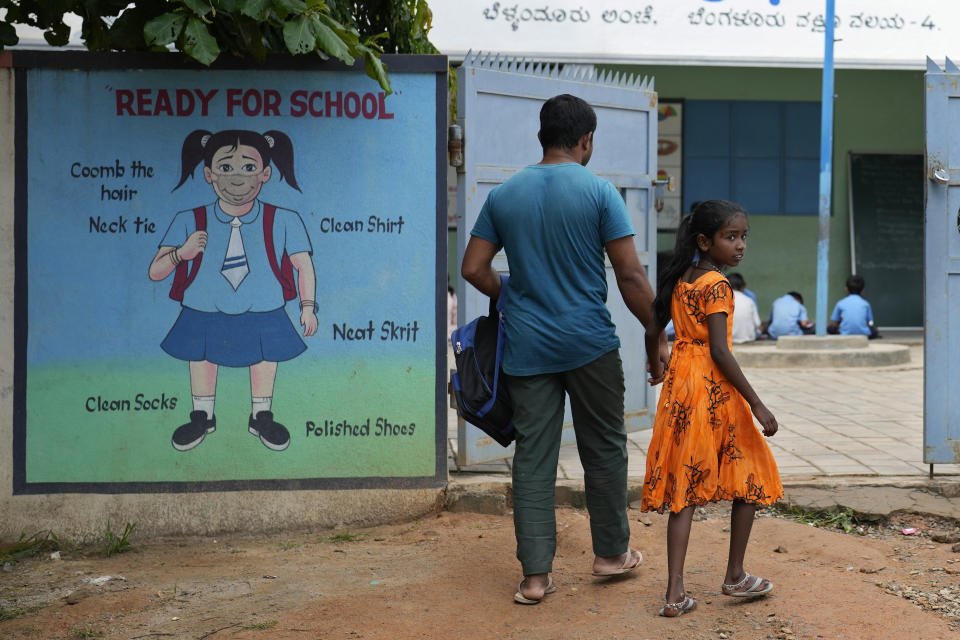 Jaidul Islam, left, arrives with his daughter Jerifa to drop her at a government school in Bengaluru, India, Wednesday, July 20, 2022. A flood in 2019 in the Darrang district of India's Assam state started Jerifa, her brother Raju and their parents on a journey that led the family from their Himalayan village to the poor neighborhood. (AP Photo/Aijaz Rahi)