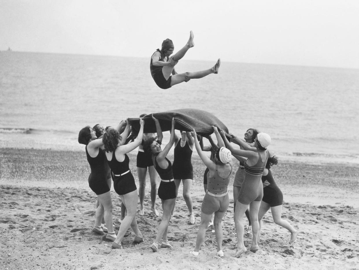 Women at the beach toss their colleague in the air with a blanket in 1932.