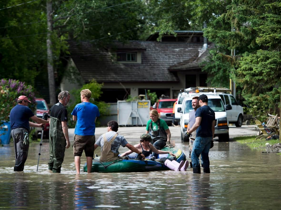 Residents and volunteers take a break in a raft as Bowness residents clean up from the city's 2013 flood. City emergency management officials say the city will soon be fully protected from that level of flood. (Nathan Denette/The Canadian Press - image credit)