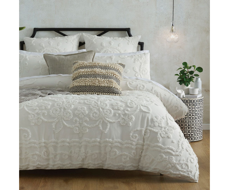 A white queen bed on wooden floors with the quilt cover showing tufted pattern work. 