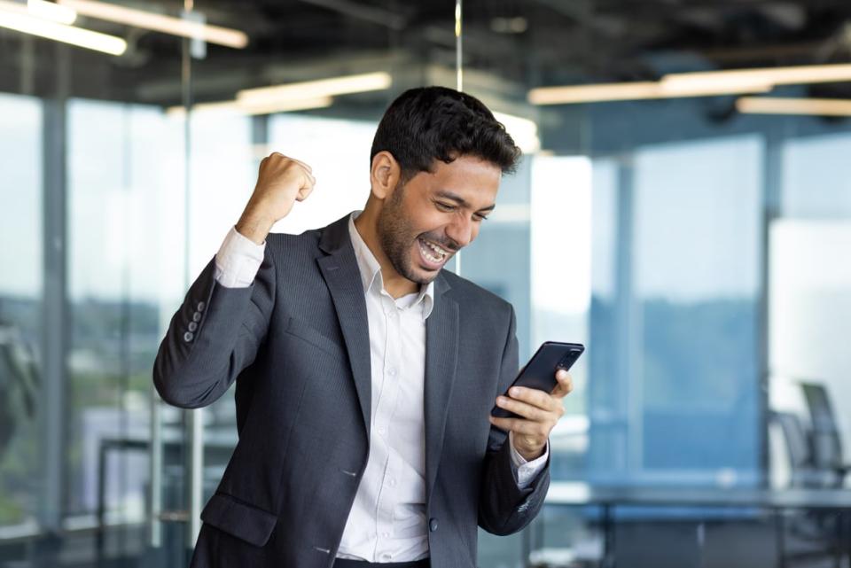 Person holding mobile device in business setting, looking very happy.